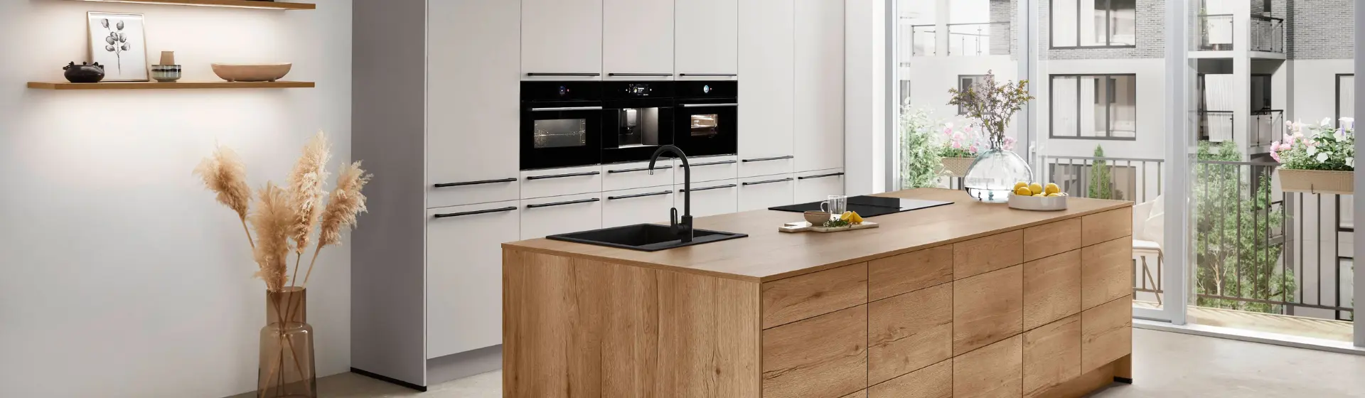 Moderne Küche mit einer Holzinsel, eingebauten schwarzen Öfen, offenen Regalen mit Dekoration und großen Fenstern, die für natürliches Licht sorgen Moderne Küche mit einer Holzinsel, eingebauten schwarzen Öfen, offenen Regalen mit Dekoration und großen Fenstern, die für natürliches Licht sorgen